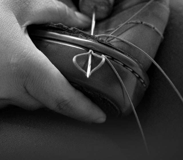 Worker hand-sewing the upper of a shoe to the sole.