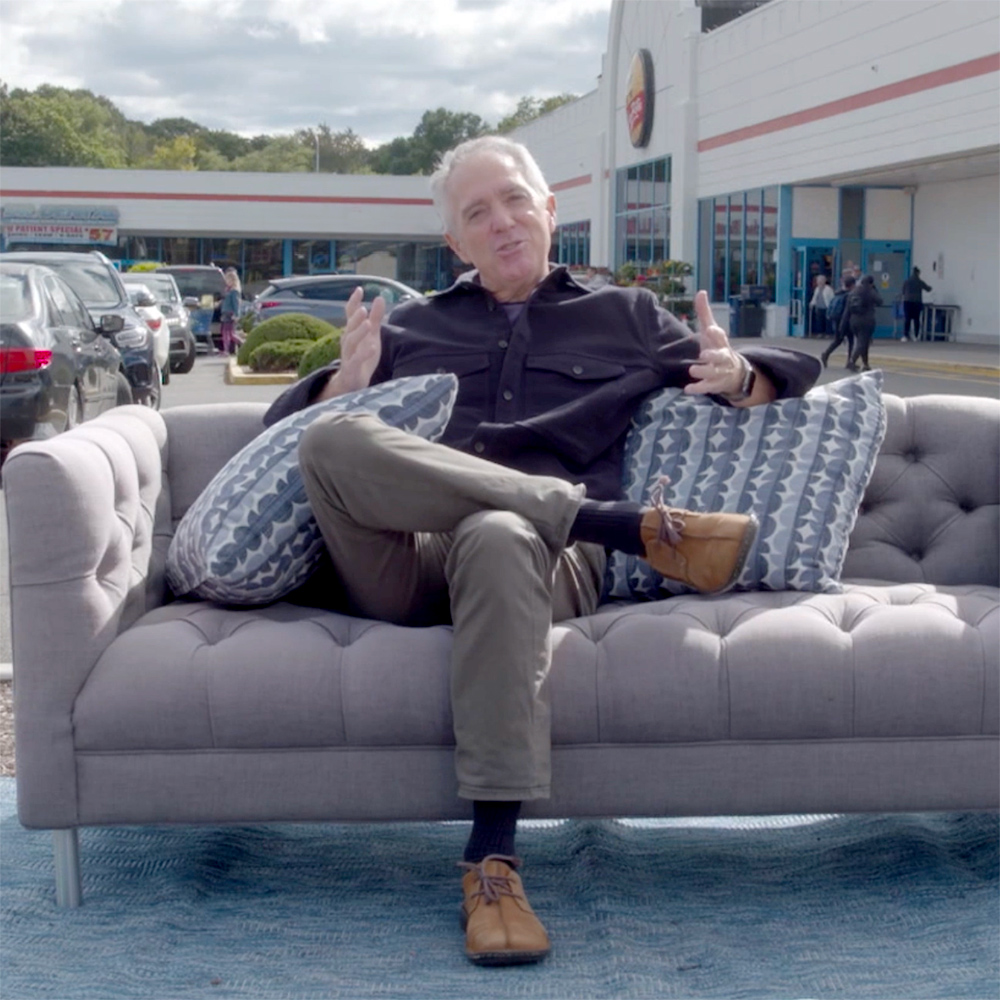 A man sitting on a sofa with a shopping mall behind him.