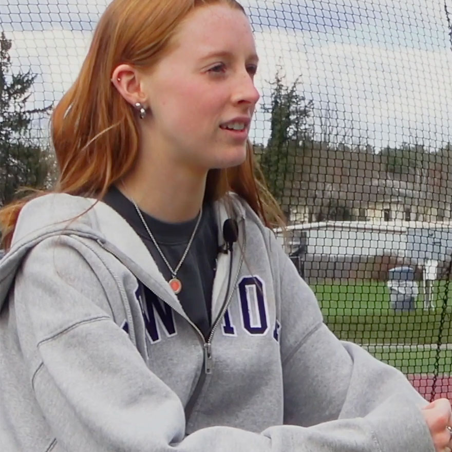 Woman sitting in an armchair with a lacrosse field behind her.